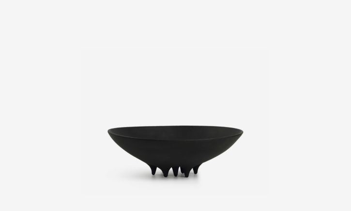 Black ceramic vase with soft oval forms and small conical legs, serving as a sculptural piece.