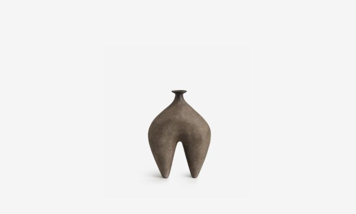 A rustic sculptural vase with a narrow neck and two curved leg-like extensions, resembling a minimalist abstract figure.